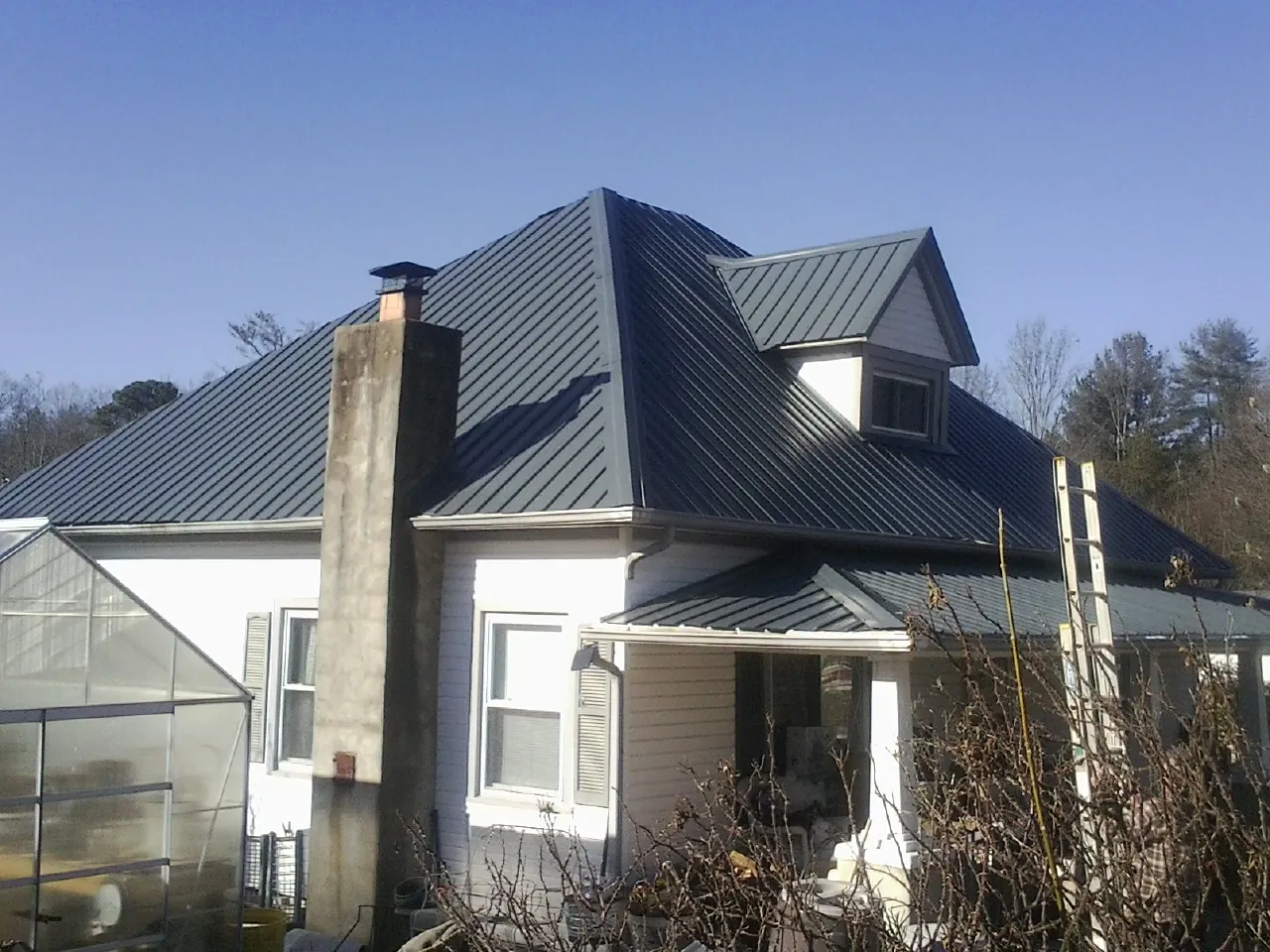 Dark blue standing seam metal roof on a white farmhouse with dormer — Slate & Tile Roof Repair by Roofing Brothers in Dodge